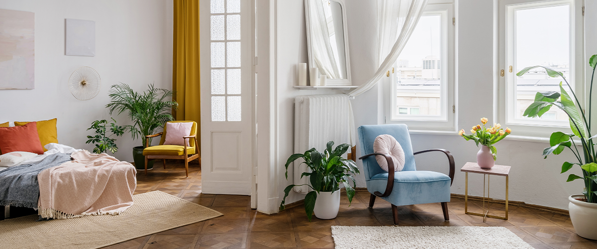 A bright and airy living room with a mix of modern and vintage furniture, colorful accents, and large windows letting in natural light.