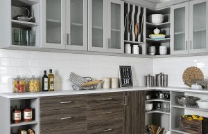 Gray kitchen cabinets with glass-front doors and brown drawer fronts in white kitchen