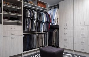 Gray closet organizer system with men's clothes and black sitting stool