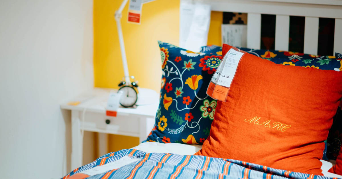 A bed with a red pillow and a night stand with a lighting fixture