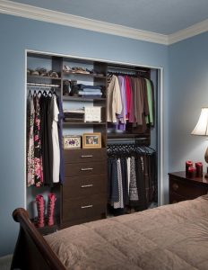 Dark wooden reach-in closet organization system with clothes hanging on racks