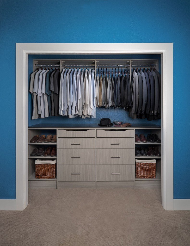 Gray wooden reach-in closet organization system with shelving and baskets, stocked with clothes and shoes
