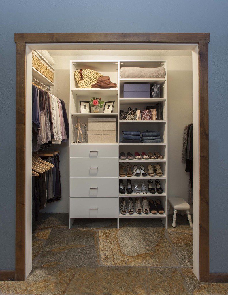 White reach-in closet organization system stocked with clothes, shoes, and accessories in illuminated closet