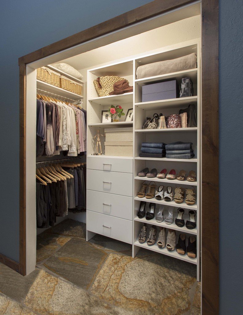 Side view of illuminated reach-in closet organization system stocked with clothes, shoes, and accessories