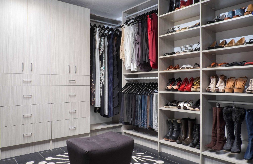 Shoes, boots, and clothes in walk-in closet system with light wooden cabinets and shelves