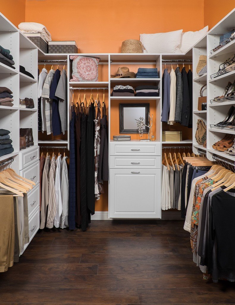 White walk-in closet organization system in orange closet stocked with clothes, shoes, and accessories