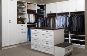 Clothing and shoes stored in closet with white organizer system comprising shelving, cabinets, and drawers