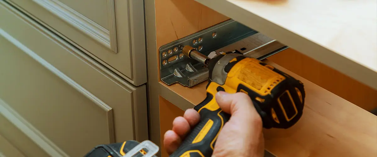 A man installing a drawer on a cabinet with a screw driver