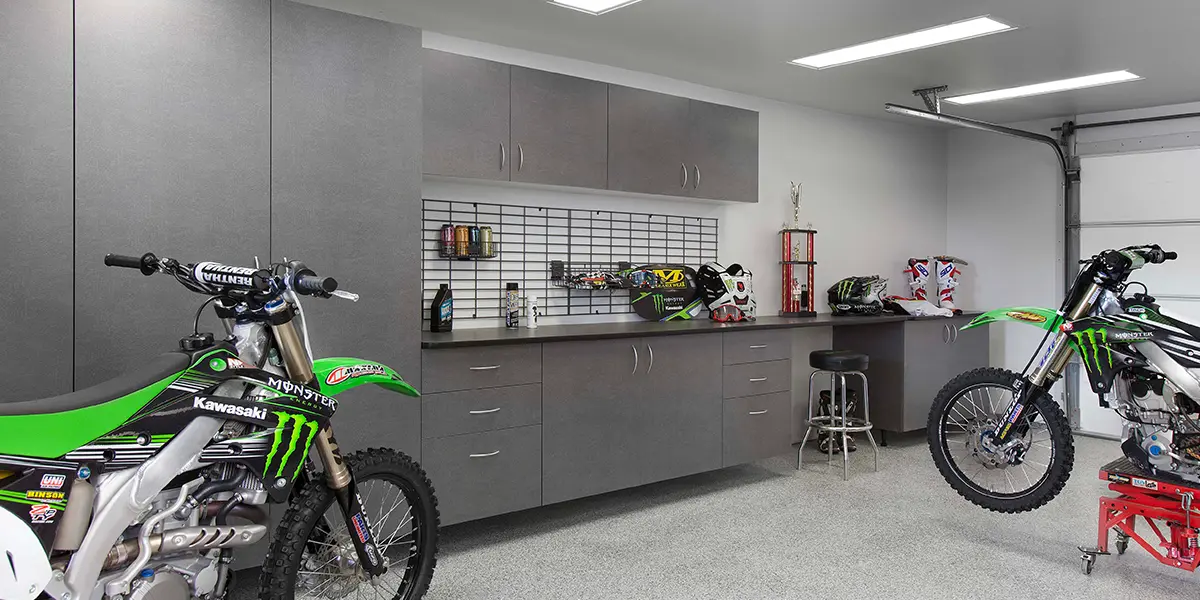 A garage with gray cabinets and two dirtbikes