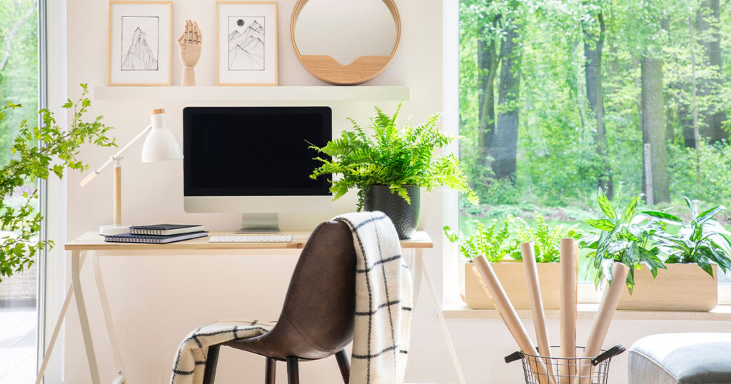 Shelves with illustrations above a wooden desk with computer by a window in a natural, white home office interior