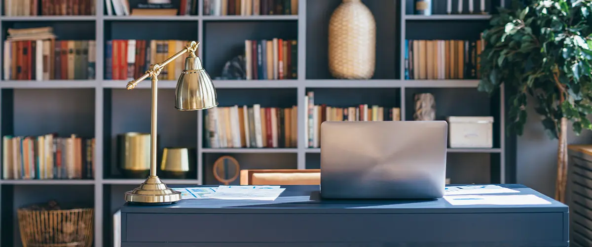 Table with laptop in home office interior with books on shelves in the back.