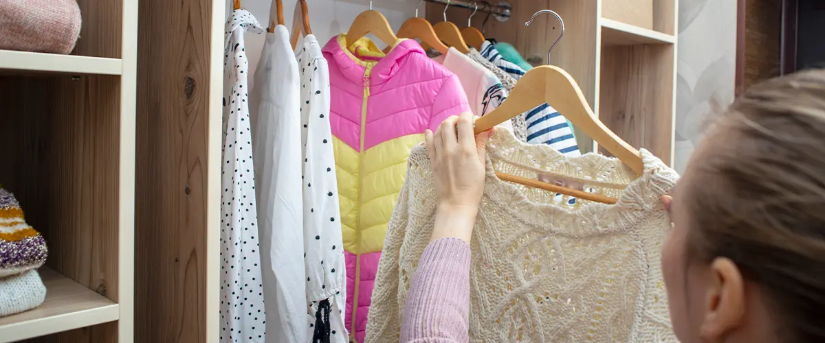 Woman choosing outfit from large wardrobe closet with stylish clothes and home stuff